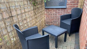 Un petit espace extérieur aménagé avec deux chaises et une table, délimité par une clôture en bambou et un mur de briques.