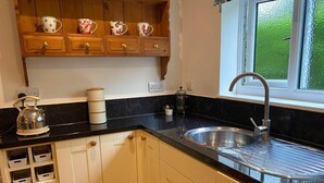 Une cuisine dotée d’un plan de travail noir, de meubles blancs, d’un évier en acier inoxydable et d’une fenêtre donnant sur un paysage verdoyant.