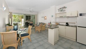 A modern kitchen with white cabinets, a microwave, and a dining area with wicker chairs and a glass table.
