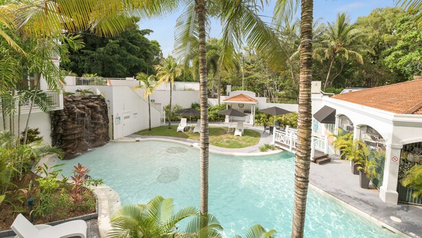 A pool area with lounge chairs, palm trees, and a waterfall feature.