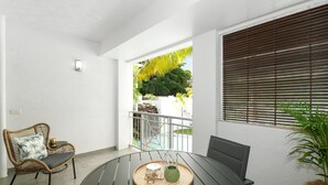 A balcony with a wicker chair, a round table with a tray, and a potted plant.