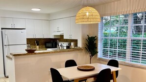 A modern kitchen with white cabinets, a central island, and a dining area with a table and chairs. - 350A - Boca Retreat w/ Pool, Parking, Near Evert Tennis & Shops (Boca Raton)