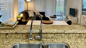 A kitchen with granite countertops, a double sink, and a hanging light fixture. - 350A - Boca Retreat w/ Pool, Parking, Near Evert Tennis & Shops (Boca Raton)