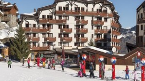 A multi-story hotel with balconies and ski slopes in the background. - Courchevel La Tania, 2-room apartment with basement parking (Courchevel)