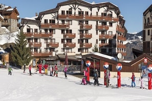 A multi-story hotel with balconies and ski slopes in the background.