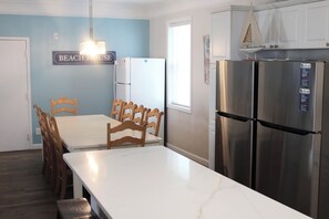 A kitchen with a white table, wooden chairs, a stainless steel refrigerator, and a sign reading "BEACH HOUSE".