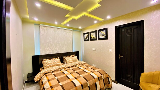 Un dormitorio con una cama, cabecera negra, sillón amarillo y una puerta.