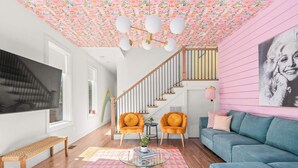 A living room with a staircase, two orange armchairs, a blue sofa, a wooden bench, and a pink patterned rug. - The Jolene • Bubbly Bar w/ Views • 5min to DT! 🍾 (Nashville)