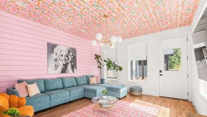 A living room with a pink wall, a blue sofa, a glass coffee table, and a geometric rug. - The Jolene • Bubbly Bar w/ Views • 5min to DT! 🍾 (Nashville)