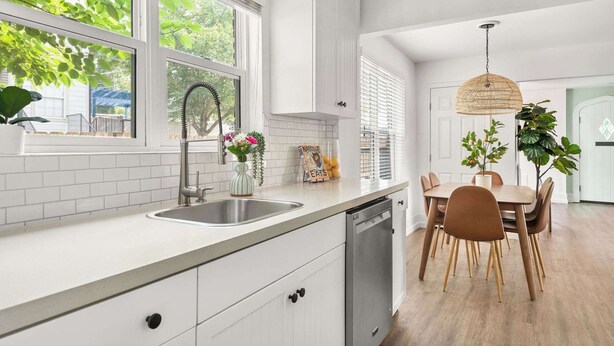 Una cocina moderna con armarios blancos, un lavamanos de acero inoxidable y un comedor con mesa y sillas de madera.