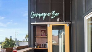 Un balcon agrémenté d’une enseigne au néon indiquant « Bar à champagne », d’un plancher en bois et de tabourets en plastique verts.