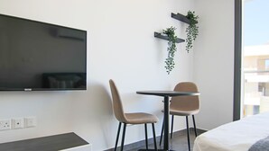 A modern hotel room with a bed, a TV mounted on the wall, a small table, two chairs, and a potted plant. - Phaedrus Living Seaside Flat Athina 116 (Paphos)