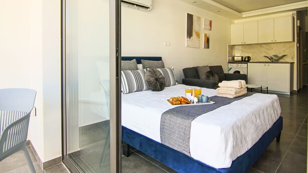 A modern hotel room with a large bed, a sofa, a dining table, and a kitchen area. - Phaedrus Living Seaside Flat Athina 116 (Paphos)