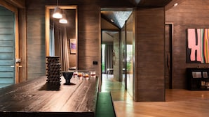 A modern kitchen with wooden cabinetry, a large island with a black bowl and glasses, pendant lighting, and a colorful abstract painting on the wall.