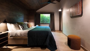 A bedroom with a wooden ceiling, a bed with a quilt, a nightstand, a lamp, a window with curtains, and a wall-mounted artwork.