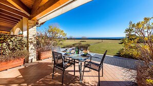 Eine Terrasse im Freien mit einem für das Essen gedeckten Tisch, mit Blick auf eine Rasenfläche und das Meer.