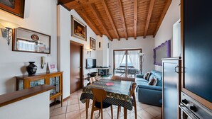 A cozy kitchen with a wooden ceiling, a dining table with chairs, a blue sofa, and a refrigerator.