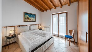 A bedroom with a bed, bedside tables, a chair, a painting, and a sliding glass door.