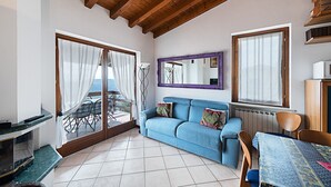 A cozy living room with a blue sofa, a dining table, and a large window with curtains.
