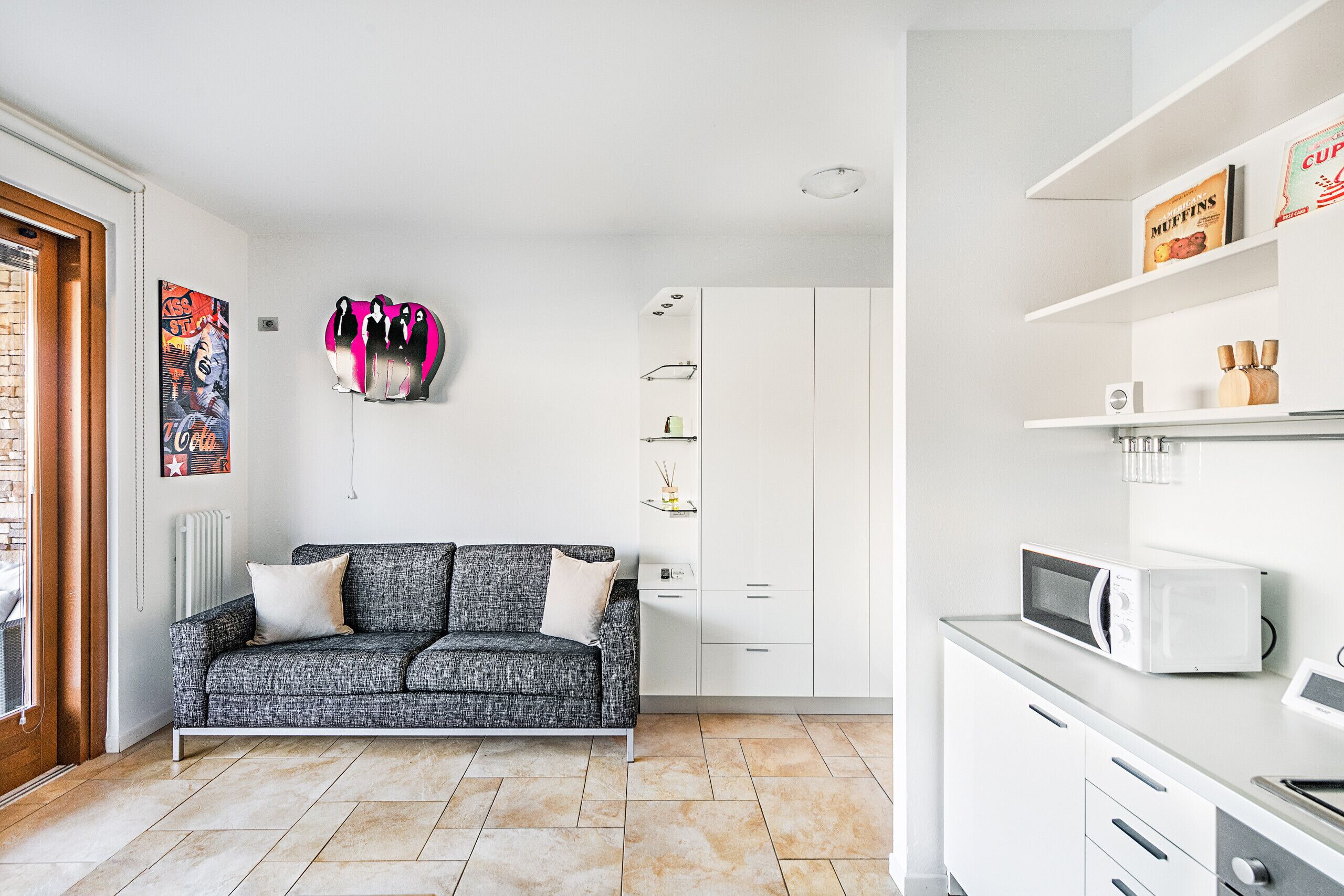 A modern kitchen with white cabinets, a grey sofa, and a microwave on the countertop.