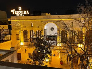 The exterior of the Tessa Hotel with a warm yellow lighting, stone facade, and an arched entrance leading to the lobby. - Tessera Hotel (Sanliurfa)