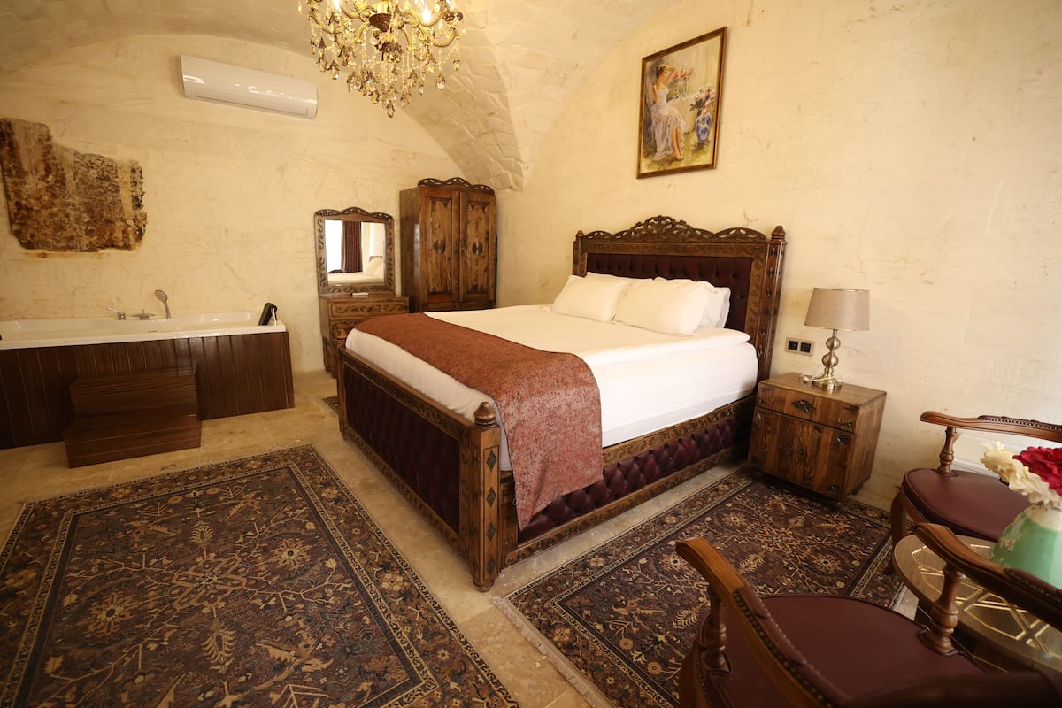 A bedroom with a large bed, a wooden dresser, a vanity with a mirror, a chandelier, and a painting on the wall.