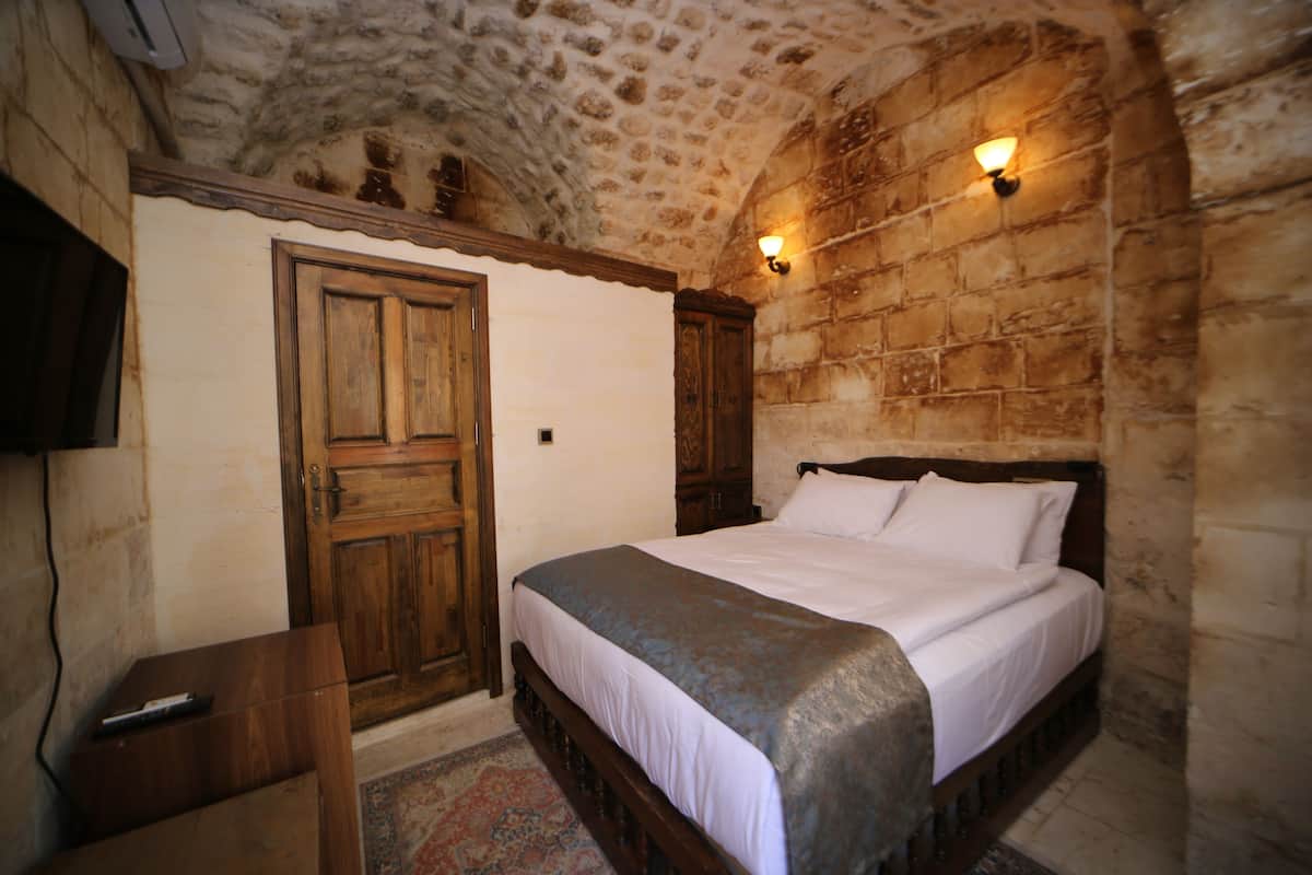 A bedroom with a stone ceiling, wooden bed frame, and a nightstand.