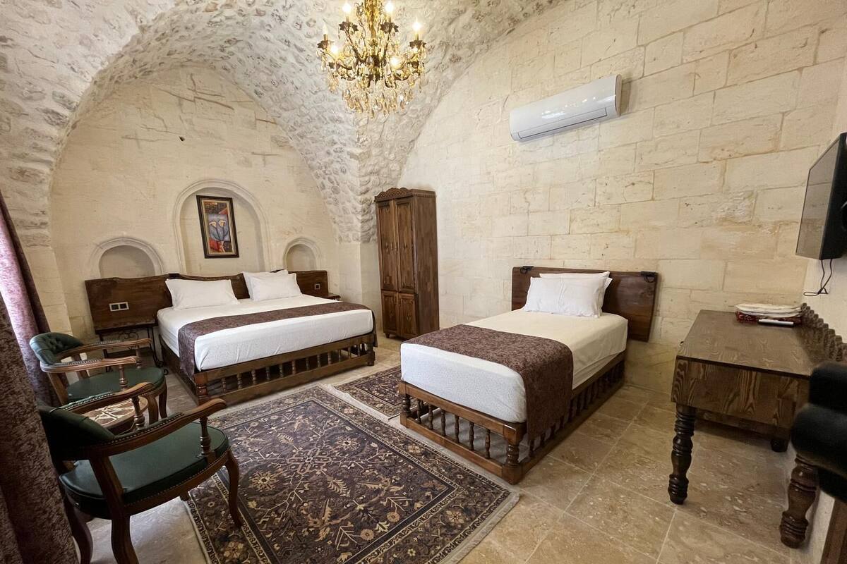 A room with two wooden beds, a chandelier, an air conditioning unit, and a television.