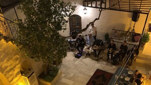 An outdoor dining area with multiple tables and chairs, surrounded by stone walls and a tree. - Tessera Hotel (Sanliurfa)