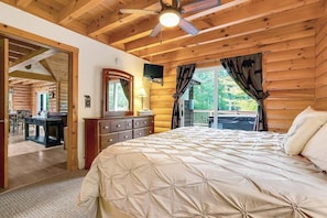 A wooden cabin bedroom with a bed, dresser, TV, and a balcony with a view.