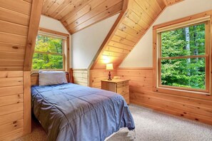 A bedroom with a bed, a nightstand, a lamp, and a window with a view of trees.