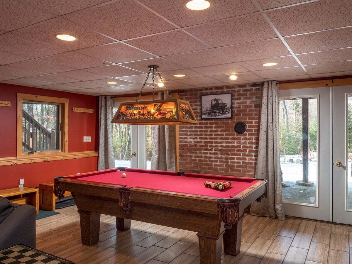 A pool table in a room with a brick wall, wooden flooring, and a window.