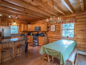 A log cabin interior with a kitchen, dining area, and a large window.