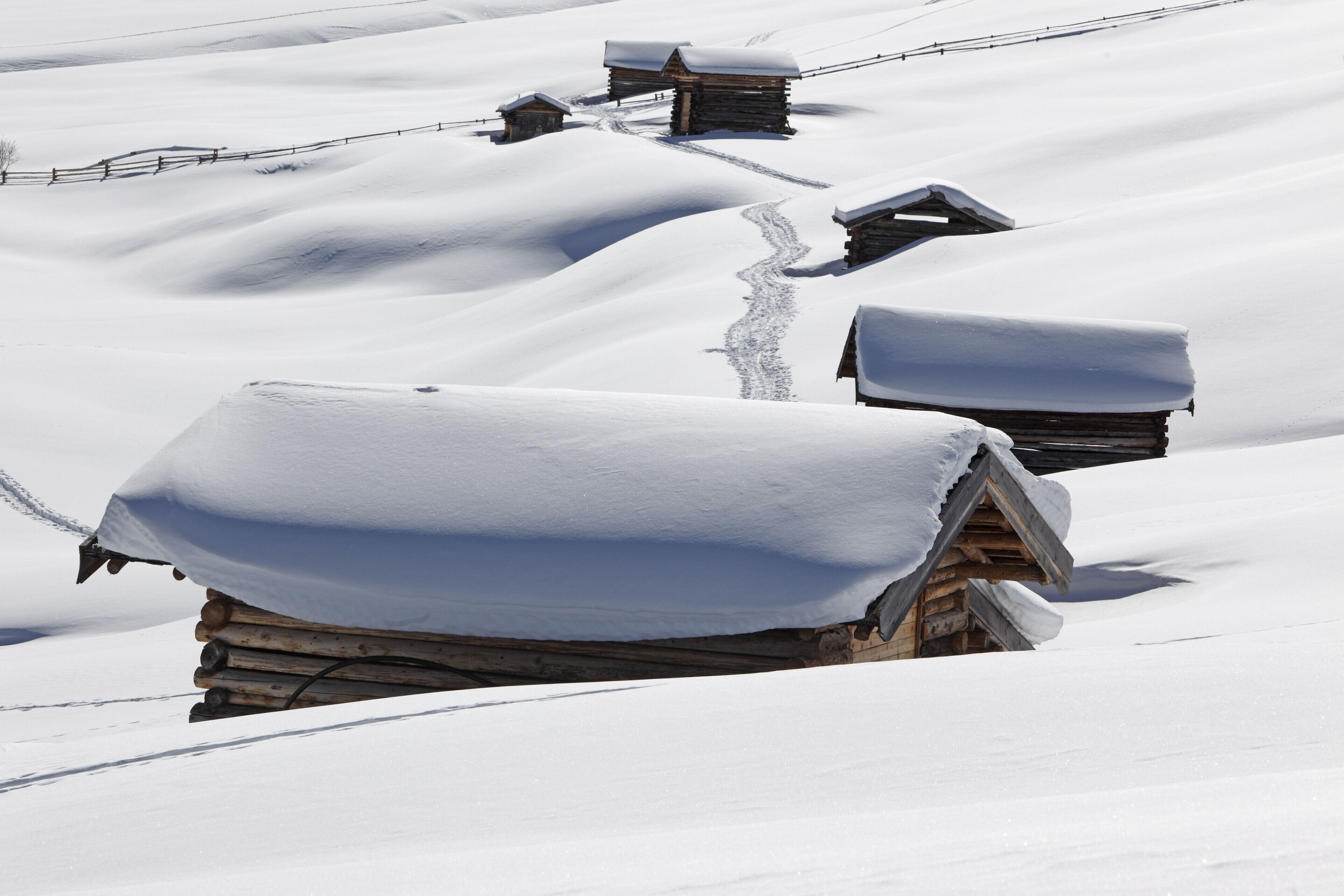 Una cabaña de madera cubierta de nieve con techo nevado, rodeada de terreno nevado y una cerca.