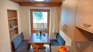 Cocina compacta con una mesa de madera, dos bancos, una pequeña barra y una ventana que da a vistas de árboles.