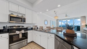 A modern kitchen with white cabinets, stainless steel appliances, and a large island with a woven basket. - Updated Luxury Beachfront Condo w/ Pool, Sauna, & Fitness Center | Sleeps 8 (Gulf Shores)