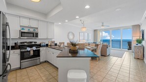 A modern kitchen with white cabinets, a central island, and a view to the outside. - Updated Luxury Beachfront Condo w/ Pool, Sauna, & Fitness Center | Sleeps 8 (Gulf Shores)