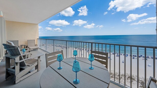 A balcony with a view of the beach and ocean, a table with chairs, and a railing. - Updated Luxury Beachfront Condo w/ Pool, Sauna, & Fitness Center | Sleeps 8 (Gulf Shores)
