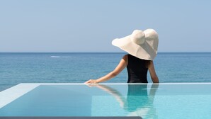 Una persona apoyada en el borde de una piscina con vista al océano.