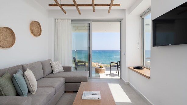 Una sala moderna con sofá, mesa de centro y televisor. Balcón con vista al mar.