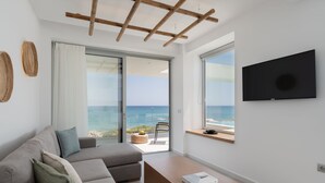 Una sala de estar moderna con sofá, una mesa de centro y televisor. Amplias ventanas ofrecen vistas al océano.