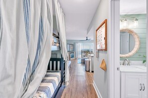 A bedroom with a canopy bed, a bathroom with a round mirror and light fixtures, and a hallway leading to a dining area.