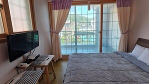 A hotel room with a bed, a TV, a desk with a chair, and a window with curtains. - Beach Getaway (Suite 201) for 1 - 3 guests: Perfect Location & Great Views. (Geoje-si)