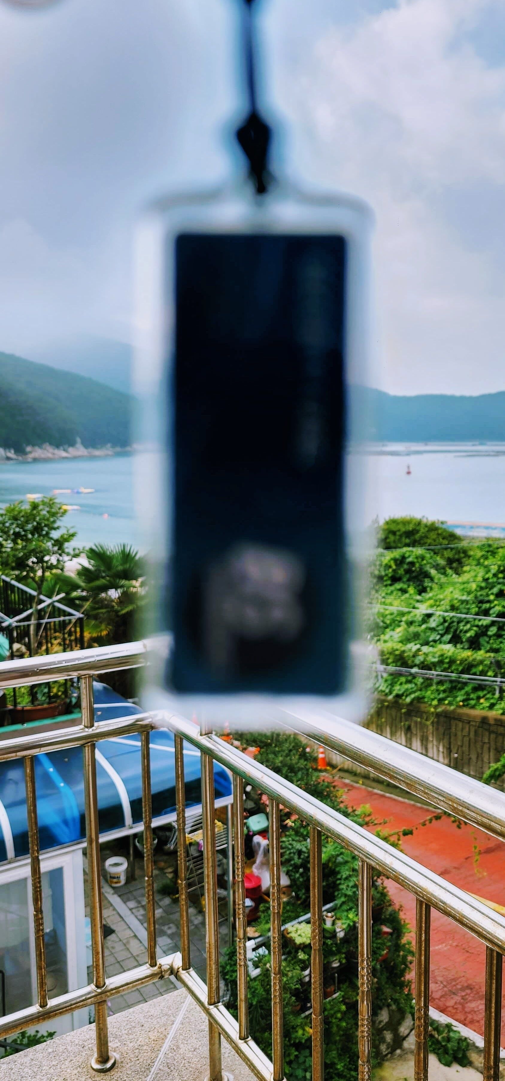 Blick von einem Balkon mit Geländer auf ein Gewässer und viel Grün.