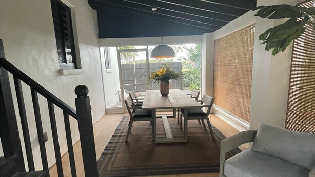 Een eethoek met een tafel, stoelen, een potplant en een trap.