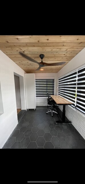 A modern room with a wooden ceiling, a black hexagonal tile floor, a table with chairs, and a window with blinds.