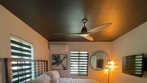 Een slaapkamer met een bed, een plafondventilator, een nachtkastje met een lamp en een tv aan de muur.
