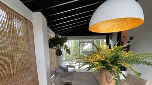 Een eethoek met een houten tafel, witte stoelen, een grote pot met een varen en een hanglamp.