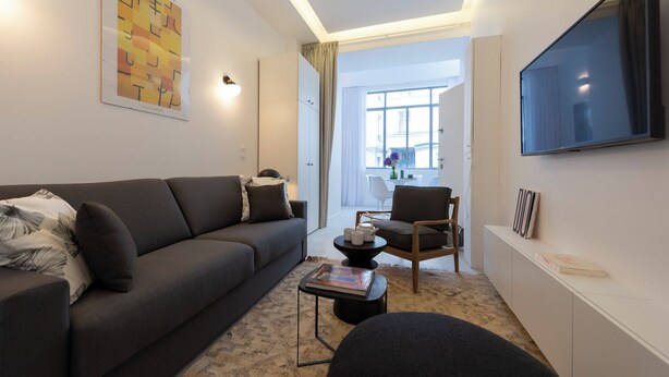 A modern living room with a grey sofa, a small round table, and a TV mounted on the wall. - Mayenne, Studio/ 1BA, 2 people (París)