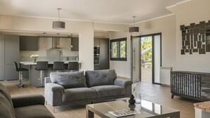 Una sala de estar moderna con un sofá gris, una mesita de centro de vidrio y una cocina al fondo.